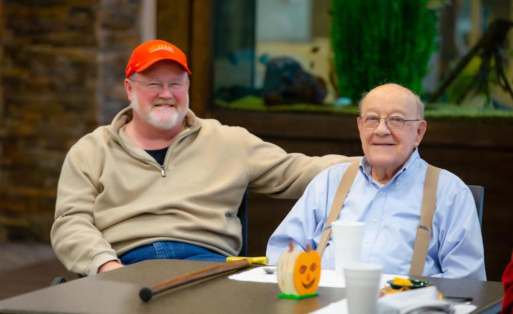 Two Men Sitting at Table Together Smiling | St. Anthony's Senior Living