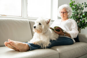 A senior citizen enjoys a book with her dog in her lap.